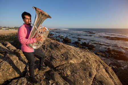 Musician play to Tuba musical instrument on romantic rocky sea shore.