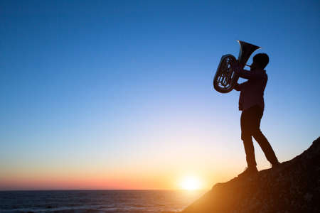 Silhouette of musician play Tuba on sea shore at amazing sunset.の写真素材