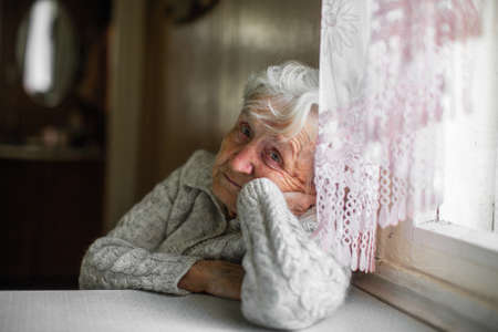 Sad old woman sitting near the window.