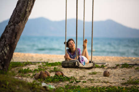 Young asian woman lies on the swings on sea beach.の写真素材