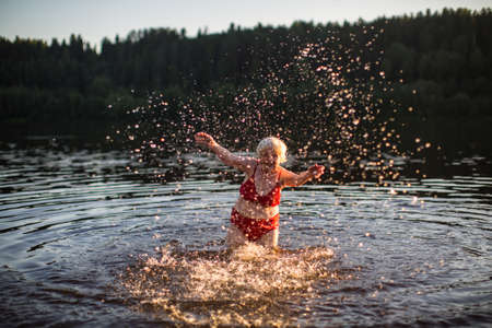 An elderly woman bathes and splashing in the river at sunset.の写真素材