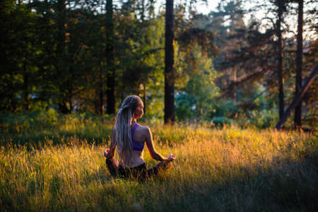 Yoga woman meditates in a clearing in the woods. Peaceful and harmony.