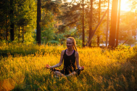 Yoga woman meditating on a picturesque glade in a green forest.