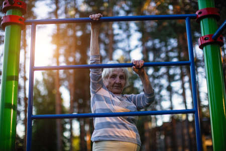 Elderly woman doing exercise on the street sport playground.