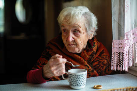 An elderly lady drinking tea sitting at a table in the house.の写真素材