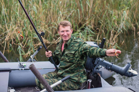 Man in camouflage fishing rod on the river on a rubber boat.の写真素材