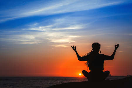 Yoga woman silhouette series. Meditation on the ocean during amazing sunset.の写真素材