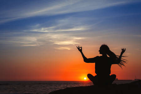 Yoga woman silhouette series. Meditation on the ocean during amazing sunset.の写真素材