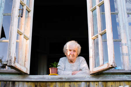 Elderly woman looks from window of a village house.の写真素材
