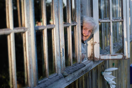 Elderly russian woman looks from window of a village house.の写真素材