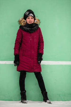 Full-length portrait near the wall of a little girl outdoors in an amazing winter.