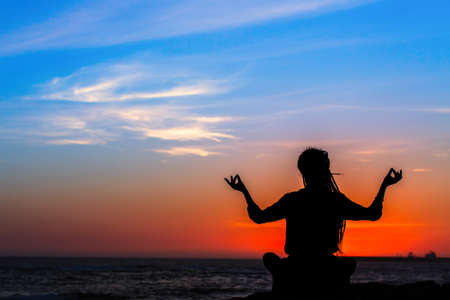 Yoga silhouette woman meditating in Lotus position on the ocean beach during amazing sunset.の写真素材