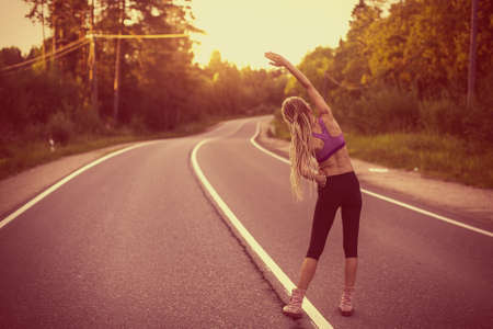 Young woman warms up before jogging on the road. Film photo effect.の写真素材
