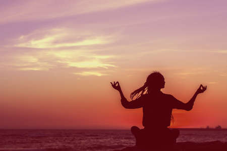 Faded photo silhouette of yoga woman meditation on the beach at sunset.の写真素材