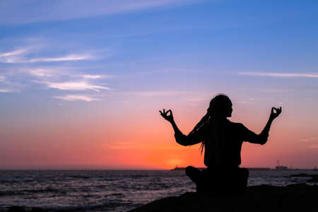 Yoga silhouette meditation woman on the Sea beach during amazing twilight.