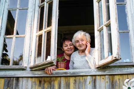 Old woman and her adult daughter from the window of village house.の写真素材