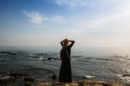 A young woman with blond dreadlocks standing on the rocks looking at the ocean.の写真素材