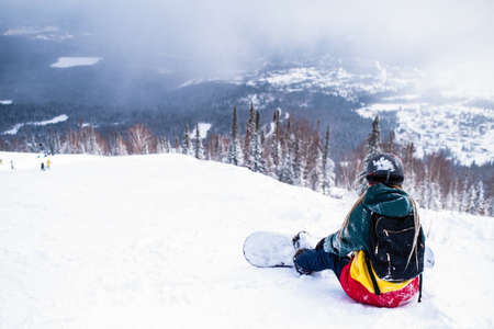 Female snowboarder freerider with snowboard in the mountains sitting on a snowy slope.の写真素材