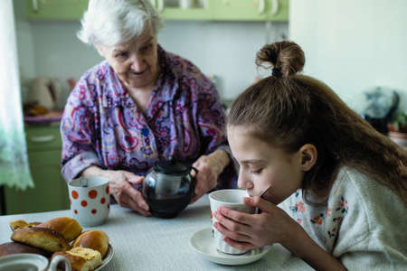 An old woman feeds her granddaughter breakfast.の写真素材