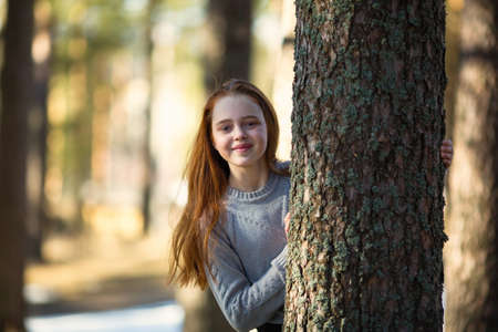 Twelve-year-old girl with long red hair posing in a summer pine Park.の写真素材