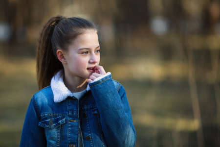 Twelve-year-old girl in a denim jacket posing in a summer pine Park.