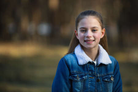 Twelve-year-old girl in a denim jacket posing in a summer pine Park.の写真素材