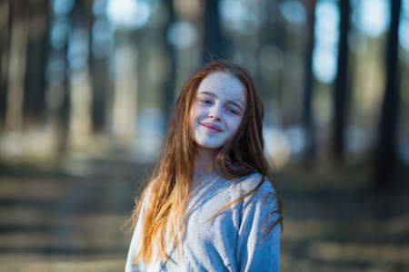 Twelve-year-old cute girl with long red hair posing for the camera in the park, photo shoot outdoors.の写真素材