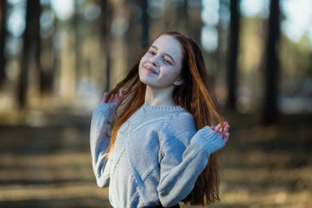Twelve-year-old cute girl with long red hair posing for the camera in the park, photo shoot outdoors.の写真素材