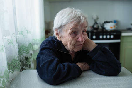 Sad elderly woman portrait near window in the house.の写真素材