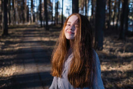 Cute schoolgirl with long red hair posing for the camera in a pine park in the summer.の写真素材
