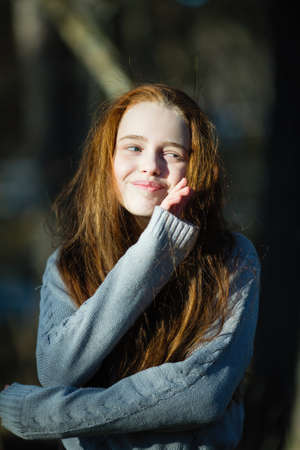 Portrait of cute twelve year old girl with fiery red hair posing in the pine park for a photoshoot.