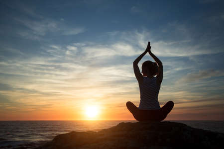 Silhouette young woman practicing yoga on the beach at amazing sunset.の写真素材