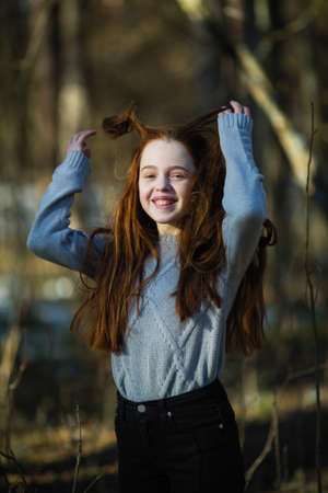 Portrait of attractive cheerful teen girl with bright red long hair, photoshooting in the spring Park.の写真素材