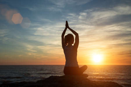 Silhouette young woman practicing yoga on the beach at sunset.の写真素材