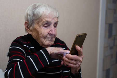 Old elderly woman pensioner typing on a smartphone.