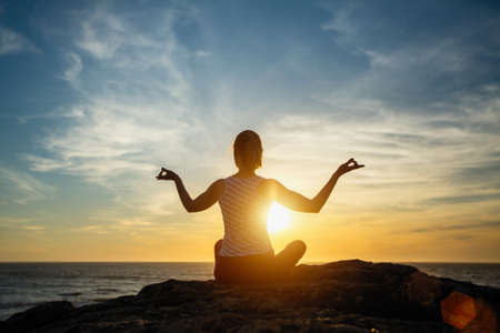 Yoga silhouette young woman doing fitness exercises on the beach at amazing sunset.の写真素材