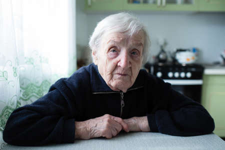 Lonely old woman sitting by the window in his cottage.