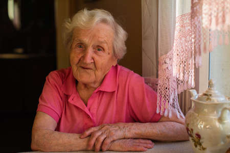 Portrait of an old woman in red clothes sitting at the table.の写真素材