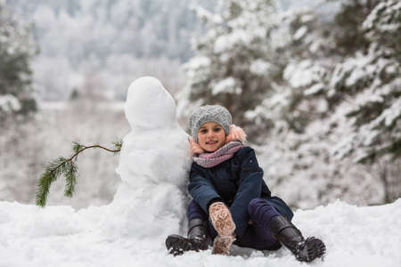 Cute little girl with snowman in winter snowy Park.の写真素材