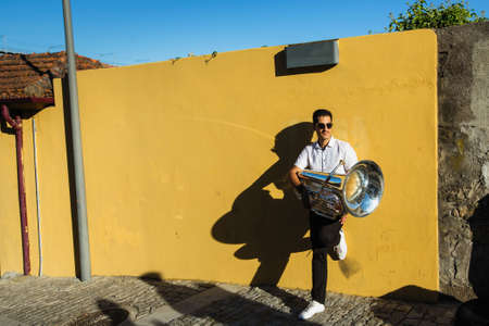 Musician with a tuba stands on the street near the yellow wall.の写真素材