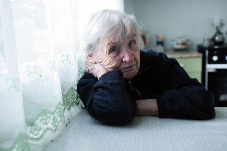 Unhappy old ledy portrait near window in the house. の写真素材