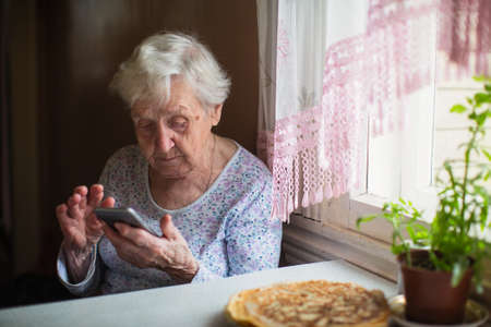 An old woman sits with a smartphone in her hands at home.の写真素材