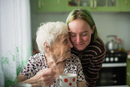 Portrait of elderly woman with her granddaughter at the table in the kitchen at home.の写真素材
