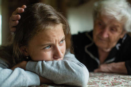 Teen girl cries, grandmother soothes and strokes her head.の写真素材