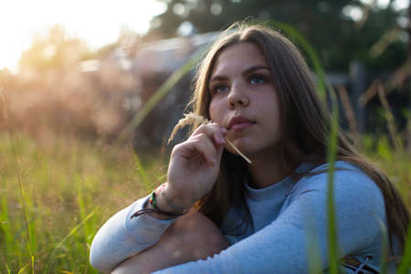 Teenage girl sitting in green grass in summer countryside.の写真素材