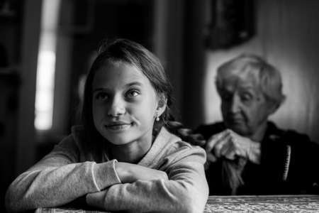 An elderly woman braids her granddaughter's hair. Black-white photo.