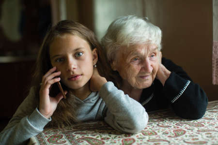 Little girl granddaughter talking on a mobile phone and grandmother her listens.の写真素材