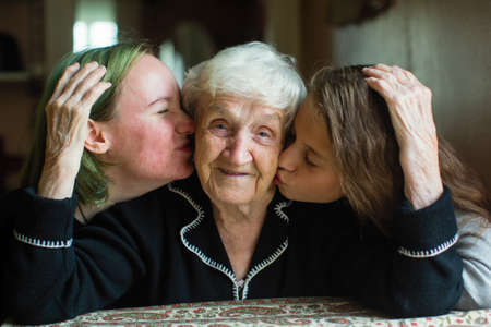 Two girls granddaughter kissing the cheeks of his old grandmother.