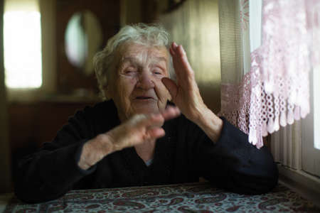 An emotional old lady tells gesturing sitting at a table in the house.