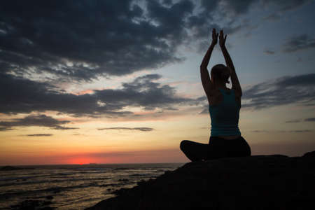 Silhouette of yoga woman meditation on the sea during sunset.の写真素材